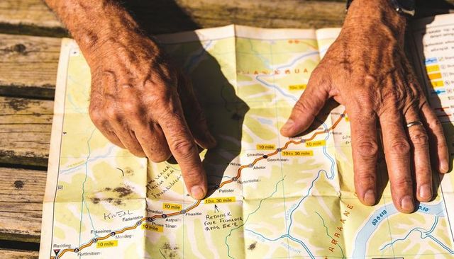 Pointing finger tracing marked route on folded map with weathered hands and watch