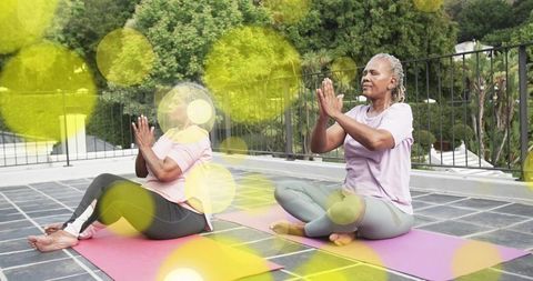 Senior women practicing rooftop yoga and meditation holding prayer pose on colorful mats