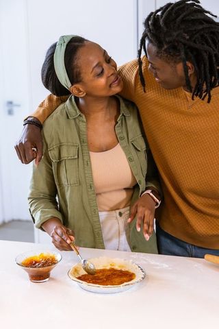 Young african american couple baking and spreading jam on pie together in cozy kitchen