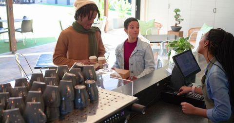 Diverse friends ordering takeaway coffee at modern cafe counter with smiling barista