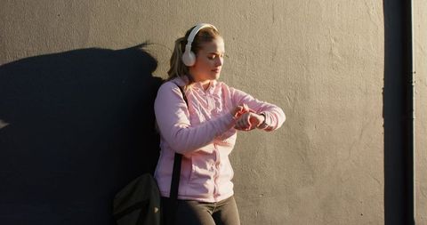 Young woman checking smartwatch while leaning on urban concrete wall during golden hour