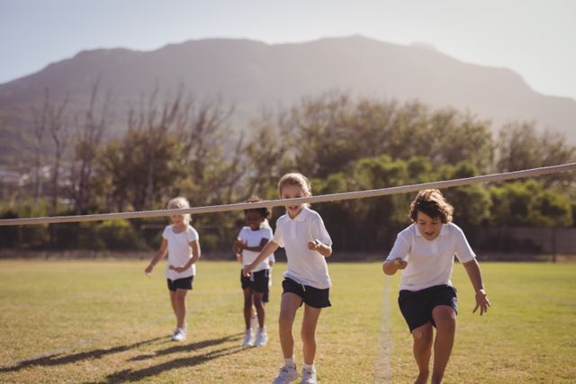 Schoolgirls are participating in an egg and spoon race in a park. They are running towards the finish line, focusing on balancing their eggs on spoons. The background features a scenic view with mountains and trees. This image is ideal for use in educational materials, advertisements for children's activities, or articles about outdoor games and physical education.
