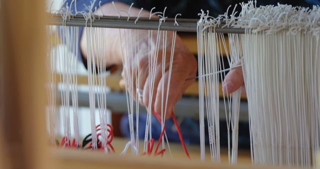 Close-up showing artisan's hands weaving on a loom with white and red threads, highlighting the skill and craftsmanship of traditional textiles. Ideal for illustrating traditional crafts, creativity, skilled labor, cultural heritage, and handmade textile products.