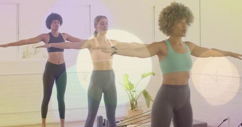 Three women practicing pilates reformer balancing arms extended in bright fitness studio