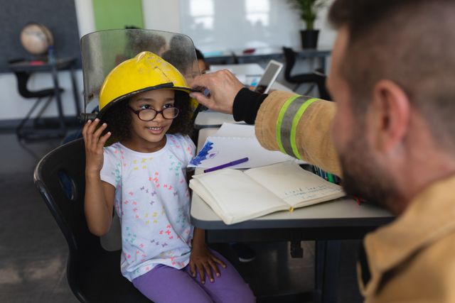 Firefighter helping a young schoolgirl wear a helmet in an elementary school classroom. This image can be used for educational materials, community outreach programs, fire safety campaigns, and promoting emergency services in schools.