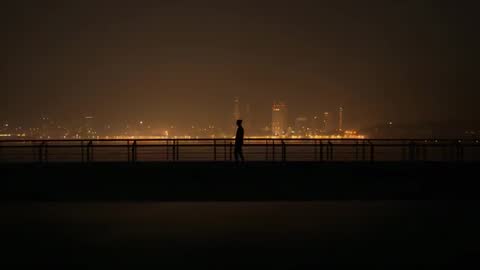Silhouette of Man Strolling on Urban Waterfront
