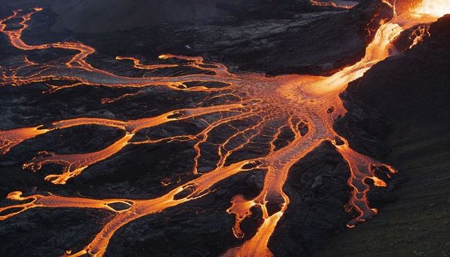 Flowing molten lava fanning across dark basalt plateau, braided magma rivers carving terrain