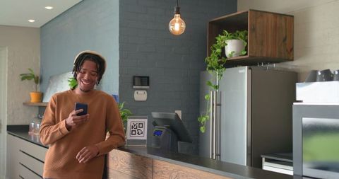 African american man leaning on cafe counter holding phone near qr code for mobile payment