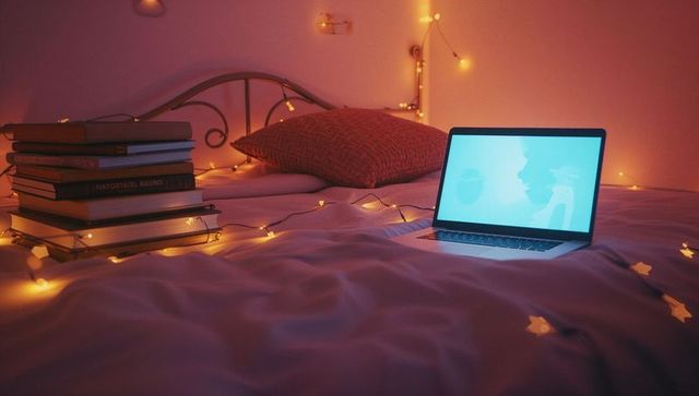 Cozy bedroom relaxation with laptop and books by string lights