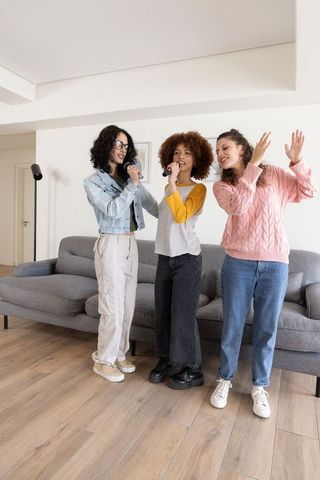 Diverse young women singing karaoke together in modern living room with casual style
