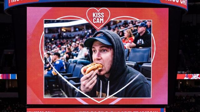 Man eating hot dog on kiss cam jumbotron during hockey game in arena