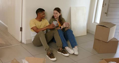 Young couple taking coffee break while unpacking in new home entryway, moving day moment