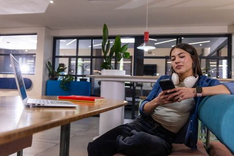 Young woman relaxing using smartphone in modern coworking lounge