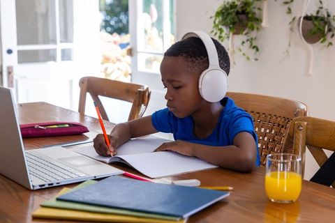 African american boy studying at home with headphones laptop notebooks and orange juice