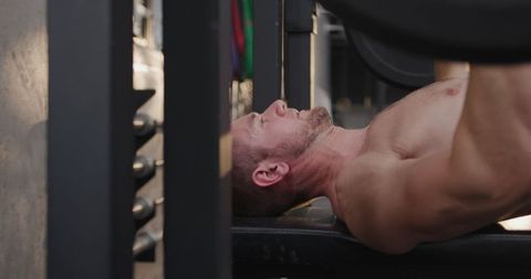 Muscular male performing barbell bench press in gym ambience