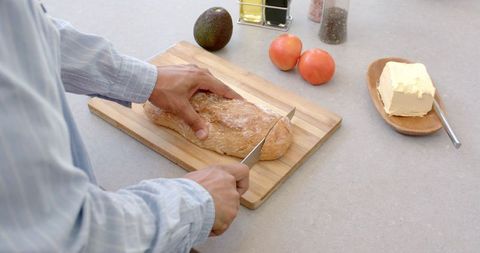 Man Slicing Bread with Fresh Vegetables in Modern Kitchen