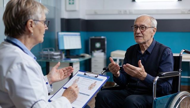 Senior man consulting doctor in wheelchair, discussing health concerns during clinic visit