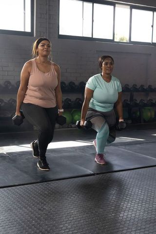 African american women performing forward lunges with dumbbells in gym