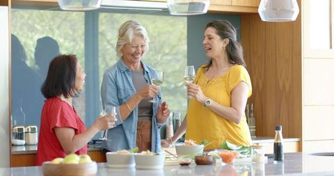 Diverse women toasting and chatting at kitchen island with wine, salad, casual entertaining