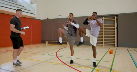 Coach leading diverse athletes through knee drills in indoor basketball training session