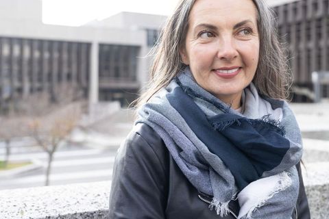 Mature woman leaning on urban railing smiling, wearing layered scarf and leather jacket