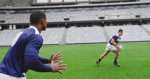 Rugby players executing fast pass on empty stadium pitch, teammates practicing attack formation