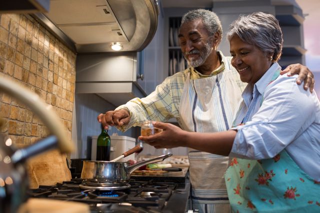 Senior couple enjoying cooking together in a modern kitchen. Perfect for illustrating themes of family bonding, healthy eating, and domestic life. Ideal for use in advertisements, blogs, and articles related to senior living, lifestyle, and home cooking.