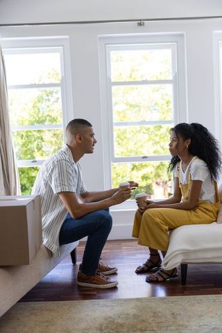 Young couple having serious conversation over coffee in new apartment during move