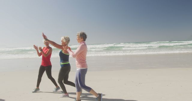 Happy senior diverse women wearing sports clothes celebrating at beach. Retirement, friendship, healthy and active lifestyle.