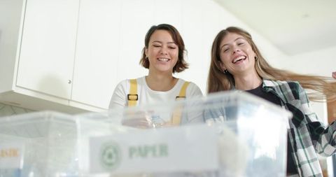 Diverse women sorting recycling in bright kitchen smiling and working together