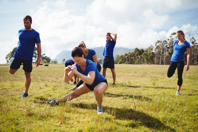 Group of people engaging in fitness training outdoors on a sunny day. They are stretching and performing various exercises on a grassy field, promoting teamwork and an active lifestyle. Ideal for use in health and fitness promotions, outdoor activity advertisements, and wellness campaigns.