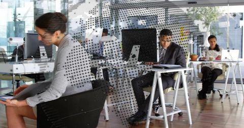 Businesswoman reviewing tablet through dotted glass partition in modern open-plan office