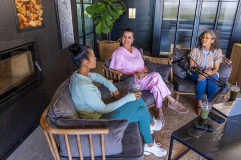 Three women recording podcast and chatting in cozy lounge with laptop and microphones
