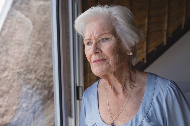 Front view of a thoughtful senior woman looking through window at home