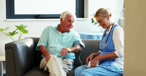 Nurse checking blood pressure for senior man on clinic sofa during wellness visit