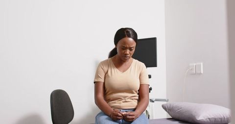 Anxious patient sitting on exam table fiddling with hands and looking down in clinic