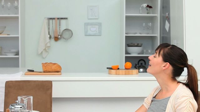 Scene shows a couple starting their morning routine, sharing breakfast in a contemporary, white kitchen. A loaf of bread on a cutting board and oranges on a dish add to the cozy atmosphere. Ideal for use in media related to lifestyle, morning routines, or culinary art.