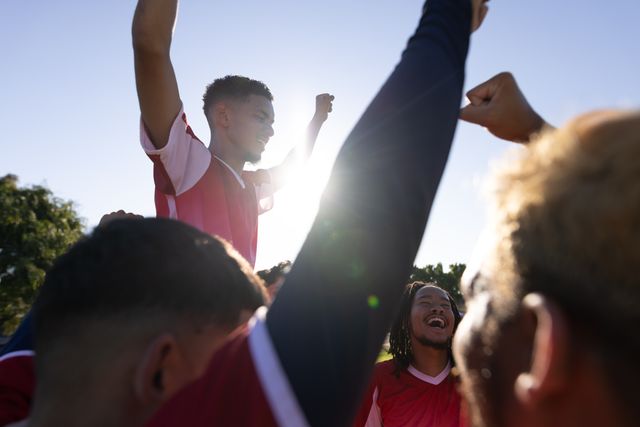 Multiracial happy players carrying teammate on shoulders and celebrating victory against clear sky. Unaltered, soccer, sport, teamwork, togetherness, competition, winning, happy and achievement.