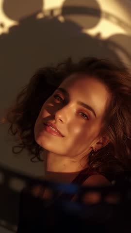 Vertical video Model blinking and tilting head in golden sunlight with moving fan shadows