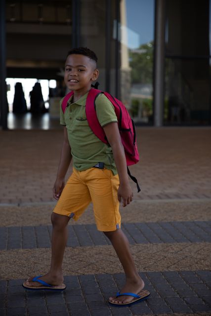Portrait of smiling african american elementary schoolboy with backpack standing at school entrance. unaltered, education, childhood and school concept.