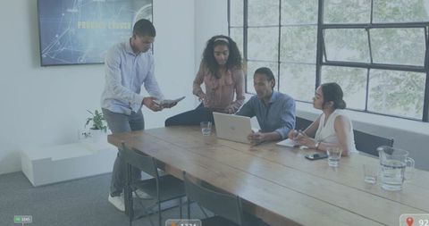 Collaborating team reviewing laptop and tablet in modern conference room with large windows