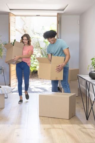 Young couple moving into new home carrying cardboard boxes through sunlit entryway