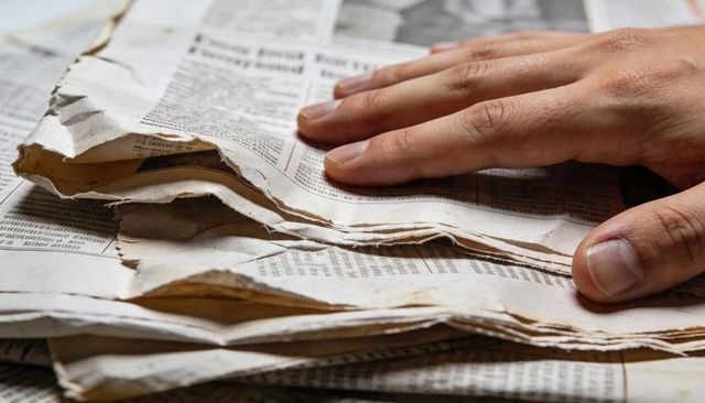 Hand resting on stacked vintage newspapers showing aged texture and newsprint closeup