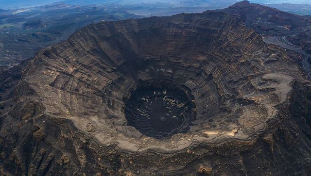 Aerial perspective revealing terraced volcanic crater with layered caldera and shadowed basin