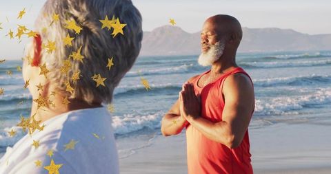 Older Black man meditating on beach at sunrise with golden star confetti, wellness and calm