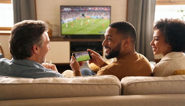 Friends watching soccer on tv sharing smartphone and snacks on cozy home couch