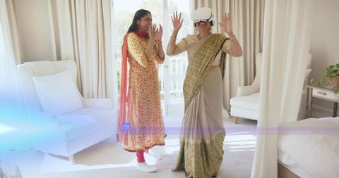Indian woman in sari experiencing virtual reality headset, relative reacting in sunlit room
