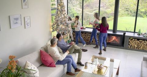 Multigenerational family decorating christmas tree in cozy modern living room by fireplace