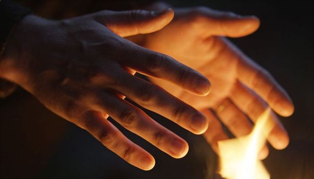 Adult hands warming over open flame at night cupping warmth candlelight glow closeup