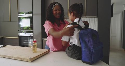 Mother Helping Daughter Adjust Backpack on Kitchen Island During Morning School Routine